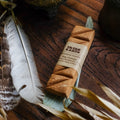 A package of Tribe Earth Nag Champa incense plank placed on a wooden surface alongside a feather and an incense holder.