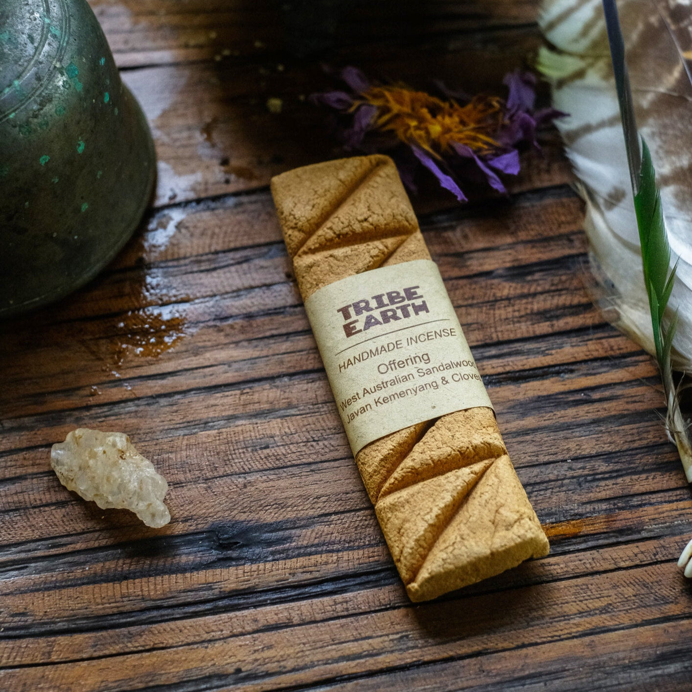Handmade incense plank on a wooden surface with a label, accompanied by a small piece of natural incense and a pot in the background.