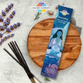 A packet of Sacred Elements GROUNDING Manifestation Incense with an illustration of a woman on it, placed next to some lavender flowers and incense sticks on a wooden board.