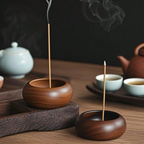 Wooden incense holders with incense sticks on a wooden table with tea sets in the background.