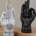 Two incense holders shaped like hands with intricate designs on a wooden surface.