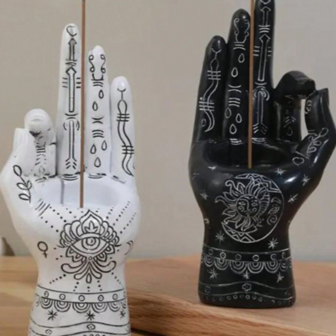 Two incense holders shaped like hands with intricate designs on a wooden surface.