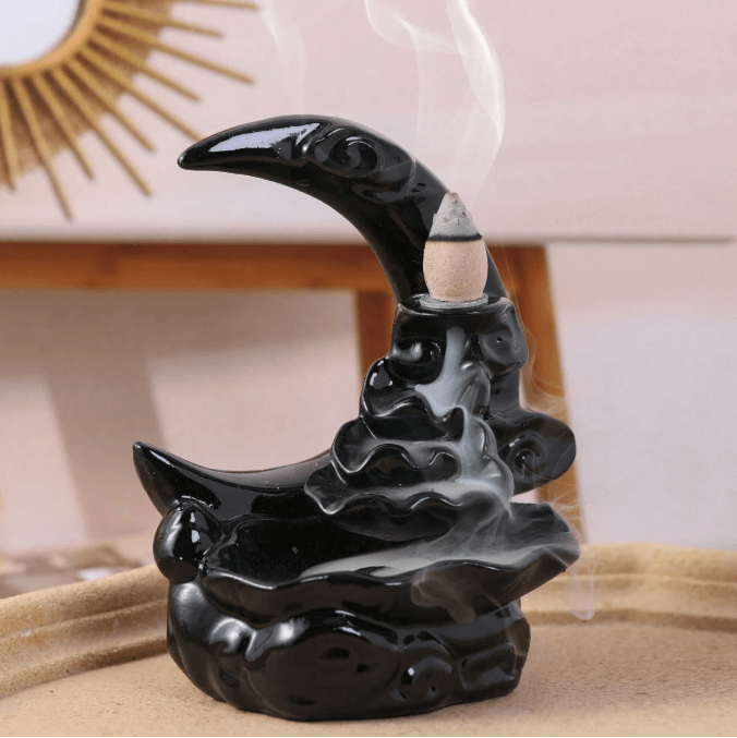 Black ceramic incense burner with smoke on a wooden surface