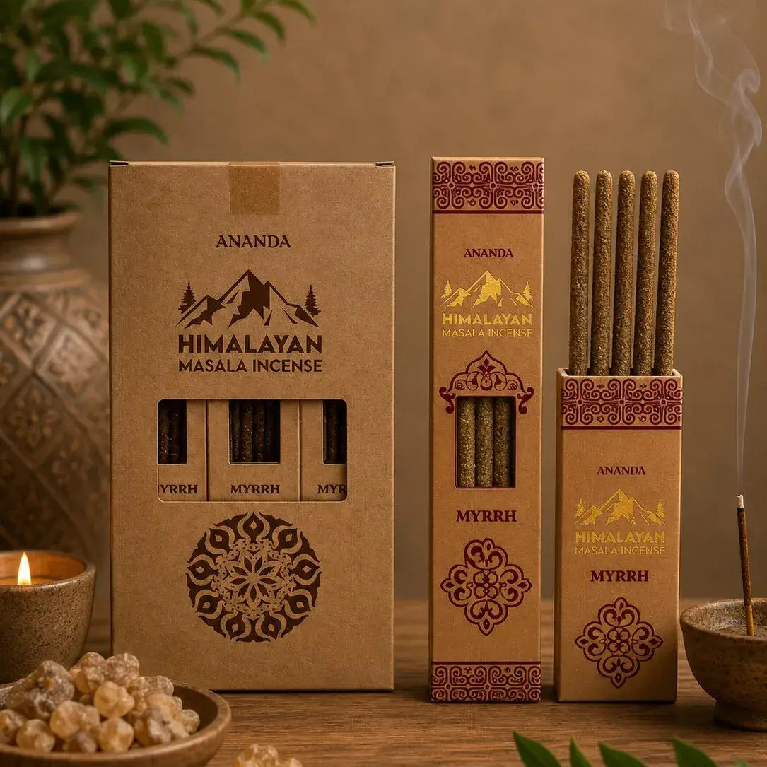 Three boxes of Ananda Himalayan Masala Ingse incense sticks arranged on a wooden surface with a lit candle, incense burner, and green leaves in the background, creating a warm, natural aesthetic.
