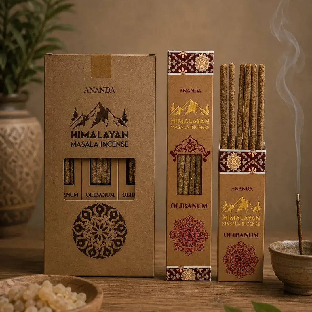 Three boxes of Ananda Himalayan Masala Incense in different sizes on a rustic wooden table, with incense sticks, a bowl of salt, and green leaves in a warm, atmospheric setting.