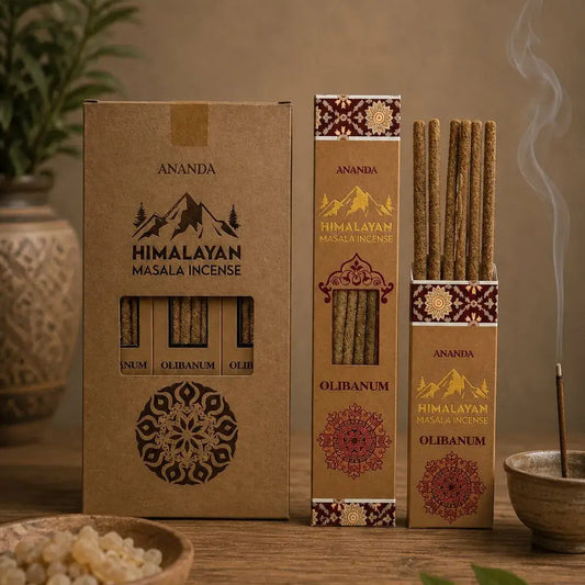 Three boxes of Ananda Himalayan Masala Incense in different sizes on a rustic wooden table, with incense sticks, a bowl of salt, and green leaves in a warm, atmospheric setting.
