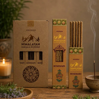 Three boxes of Ananda Himalayan Masala Incense on a rustic wooden table, surrounded by a lit candle, fresh rosemary, lavender, and a smoking incense stick in a bowl.