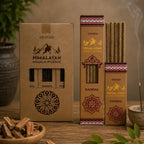 Three boxes of Ananda Himalayan incense sticks arranged on a wooden table, with one open box showing the incense sticks inside. A small bowl of wood chips, green leaves, and a smoking incense holder are placed around it in a styled setting.