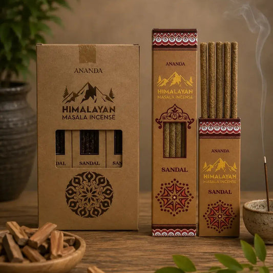 Three boxes of Ananda Himalayan incense sticks arranged on a wooden table, with one open box showing the incense sticks inside. A small bowl of wood chips, green leaves, and a smoking incense holder are placed around it in a styled setting.