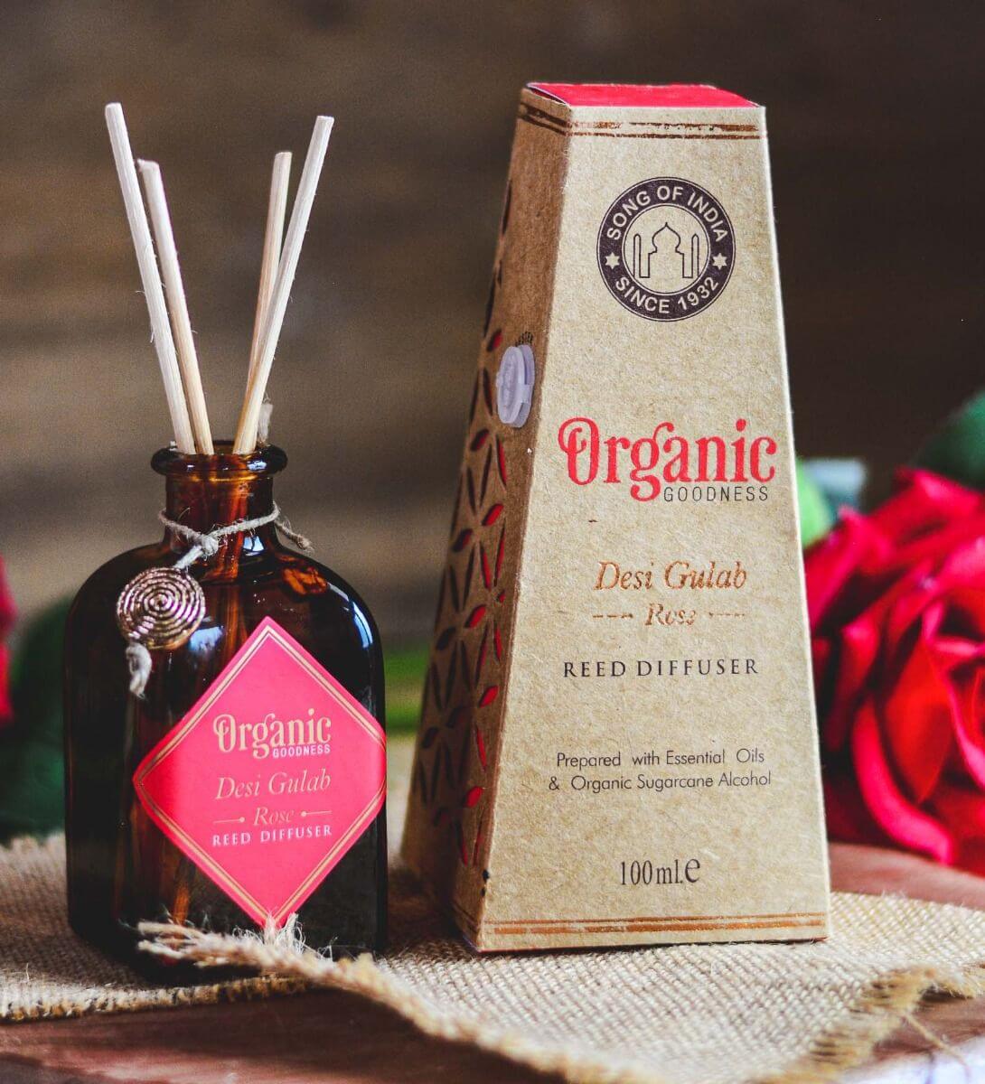 Reed diffuser bottle and packaging with a red rose in the background